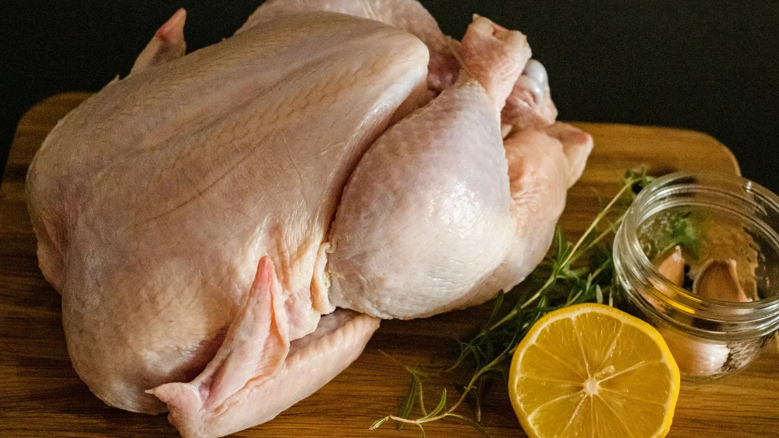 Celé syrové kuře na dřevěném prkénku, vedle půlka citronu, tymián a sklenice s česnekem