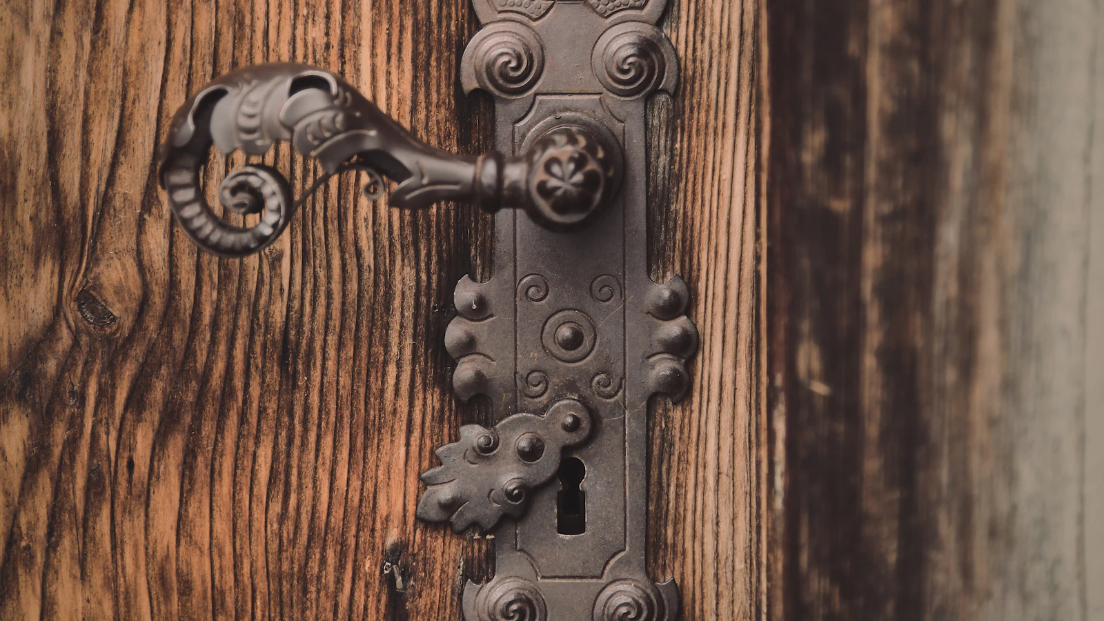 Detail černé kovové kliky na hnědých dřevěných dveřích