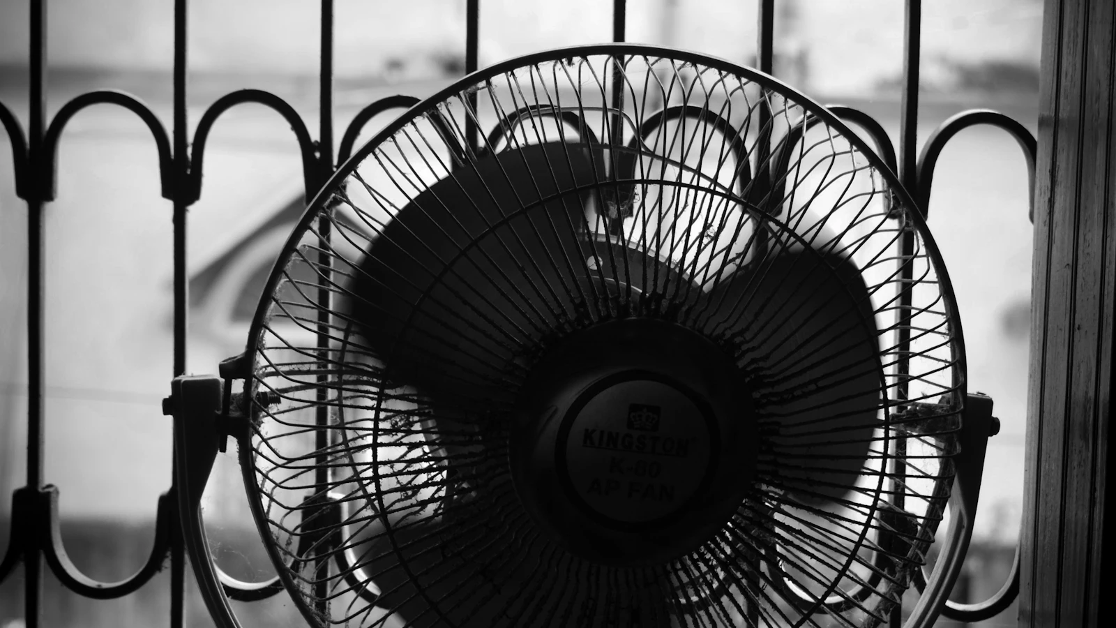 Šedý stojanový ventilátor u otevřeného okna v letním pokoji